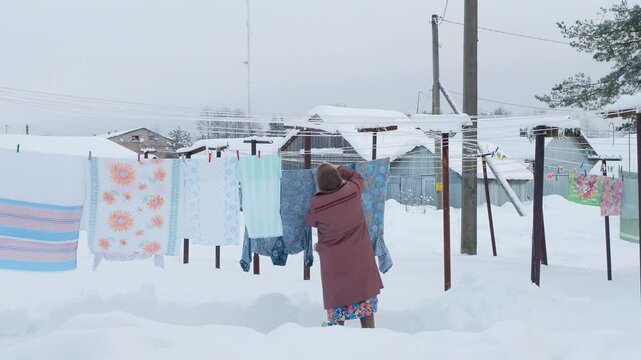 Traditional daily life far from civilization, Grandmother gray downy shawl, felt boots goes hang out laundry washing cold. Clean sheets, freshness winter snow outback, wooden village Russia, Siberia