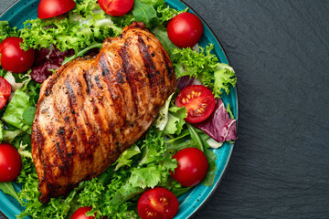 Grilled chicken breast ( fillet ) with lattuce salad and cherry tomatoes . Top view
