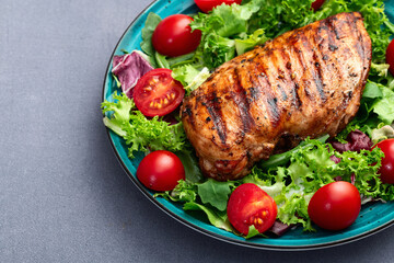 Grilled chicken breast ( fillet ) with lattuce salad and cherry tomatoes . Top view