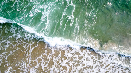 Aerial view of ocean waves crashing on a sandy beach, evoking tranquility and the spirit of summer vacations