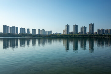 Naklejka premium Waterfront cityscape in Liuzhou, Guangxi, China. Calm river reflecting the skyline of modern residential buildings along the riverbank.Concept of urban development the issue of apartment oversupply.