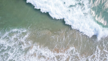 Aerial view of ocean waves crashing on a sandy beach, evoking tranquility and summer vacation vibes