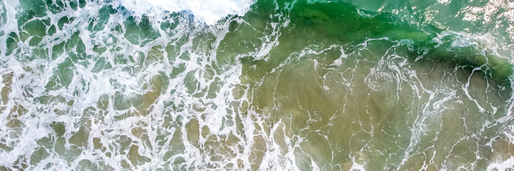 Aerial view of ocean waves crashing on a sandy beach, representing summer vacations and environmental conservation concepts