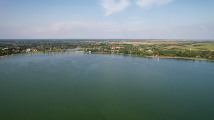 Aerial view of a tranquil lake surrounded by lush greenery and distant farmlands, embodying peaceful nature escape during summer vacation