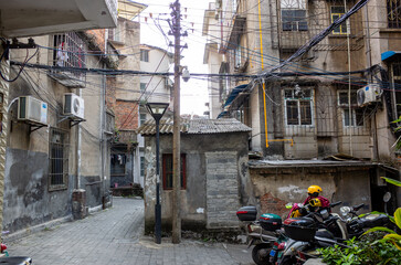 a crowded, urban alleyway in a low-income neighborhood in Liuzhou, China.The narrow passageway is lined with aging, run-down, neglected apartment buildings. Electrical wires cluttered overhead. 