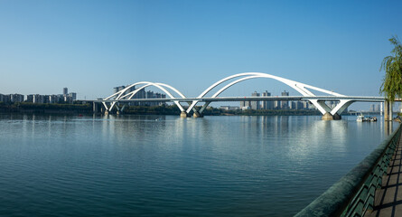 Obraz premium The panoramic view of the modern Guangya Bridge features elegant double white arches over a calm river. Liuzhou, China. Modern cityscape with transport infrastructure along beautiful riverbank.