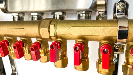 Close-up of a brass plumbing manifold with red valves for water distribution and system efficiency,...