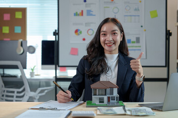 Asian saleswoman, real estate agent holding model house and writing lease contract, insurance,...