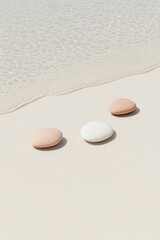 Obraz premium A beautiful arrangement of three smooth, colorful pebbles on a sandy beach, paired with clear water that adds a serene touch to the composition.