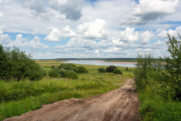 Rural landscape - dirt road against the background of a river under a cloudy sky