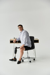 Man with a prosthetic leg sits confidently at a modern desk, dressed casually in a button up shirt.