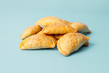 Freshly baked samsa pies with chicken sprinkled with sesame seeds on blue background, central asian cuisine, copy space.