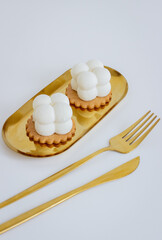Two White Dessert Cubes on a Gold Stand with Golden Cutlery on a White Background