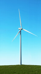 Fototapeta premium Majestic white wind turbine standing tall in green meadow under clear blue sky showcasing renewable energy technology with copy space