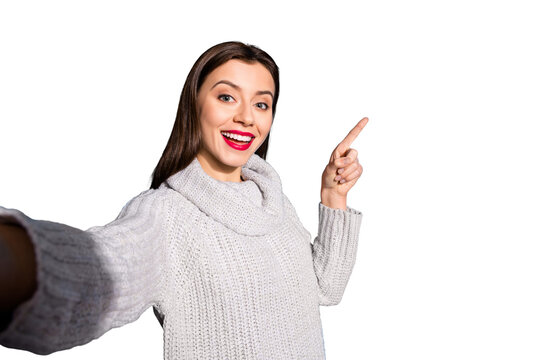 Photo of pretty lady making selfies indicating arm empty space wear warm knitted pullover isolated blue background