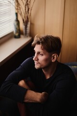 Fototapeta premium Close-up portrait of handsome young Caucasian man emotionless expression serious face against apartment background