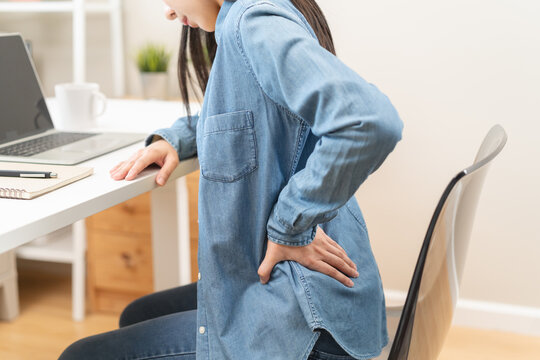 Close-up woman massaging her lower back has back pain because of sitting posture during work in office.