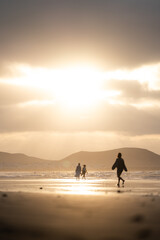People walking along the beach during sunset with mountains in the background