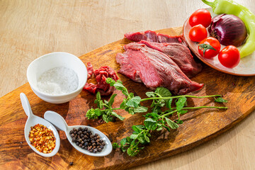 Raw beef meat on wooden cutting board with herbs and spices ready for cooking