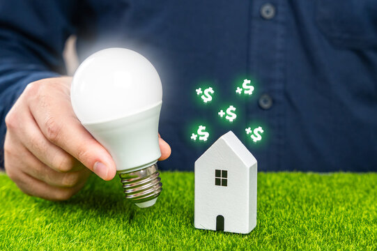 Save electricity at home and gain money. Utilities services. Save on bills. A man holds a glowing light bulb near a house.