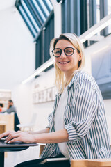 Portrait of cheerful female blogger 20s in stylish spectacles smiling at camera during network...