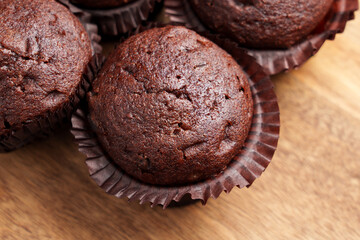Chocolate muffins with rich texture and glossy tops. Placed in brown paper liners on a wooden surface. 