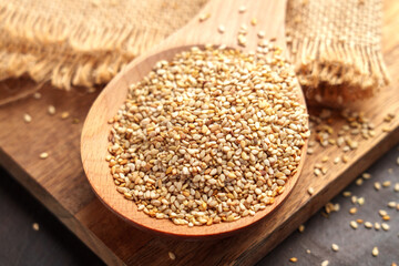 Organic sesame seeds in wooden spoon placed on rustic boards. Burlap fabric in the background. Close-up