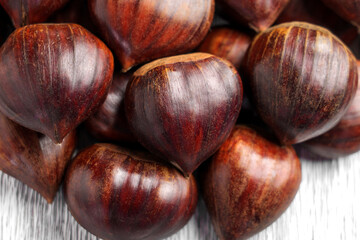 Pile of unshelled organic chestnuts with brown shells and natural texture. Close-up shot on a cracked textured light wooden background