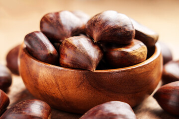 Rustic organic whole chestnuts filled wooden bowl and scattered on brown board around. Close-up. Front view