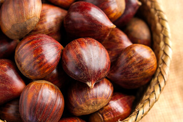 Obraz premium Brown chestnuts with textured shells in a woven basket. Freshly harvested from an organic farm