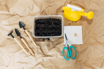 Kraft paper background, fertile soil and garden tools on top, top view. Planting seedlings in spring