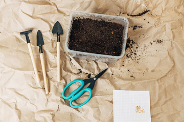 Kraft paper background, fertile soil and garden tools on top, top view. Planting seedlings in spring