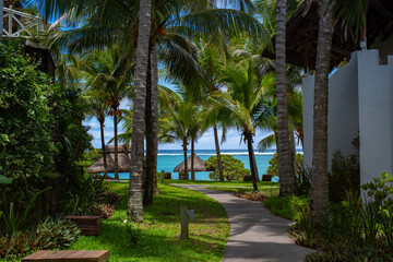 Obraz premium Vacation concept - Path near the cozy cottage. Turquoise Indian ocean and beach in a background. Vacation in a luxury island. Selective focus, blurred background. Belle Mare, Mauritius.