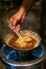 Sapporo ramen noodle lifted up by red chopsticks with steam against black background