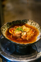 Sapporo ramen noodle lifted up by red chopsticks with steam against black background