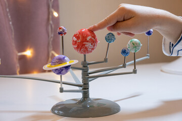 child points his finger at the sun on a homemade model of the solar system. Preschooler child is making a solar system project. A child makes a craft on the subject of astronomy. © Galina