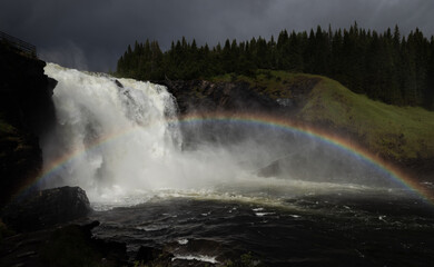 Sweden Tannforsen waterfall panorama with a rainbow in the mist. Dark, cloudy skies above