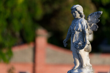 Stone sculpture or statue of a child angel, or cherub, dropping flowers in a cemetery, partially sunlit late in the day