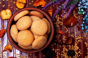homemade cookies in a clay plate, wheat, dried fruits, herbs and berries on a brown background