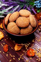 homemade cookies in a clay plate, wheat, dried fruits, herbs and berries on a brown background