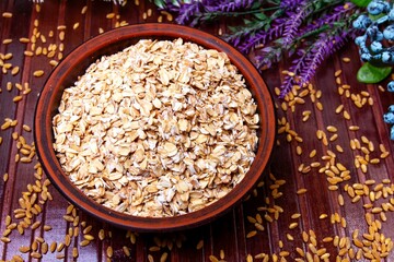 oatmeal in a clay plate, wheat, herbs and berries on a brown background