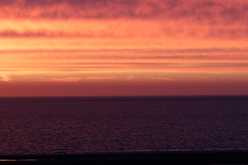 Obraz premium Sunset over a calm sea. Vibrant hues of orange and red paint the sky, reflecting on the dark water. Tranquil scene.