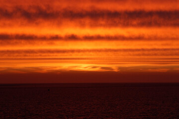 Fiery orange sunset over dark water.  Silhouette of a buoy on the horizon. Dramatic colors.