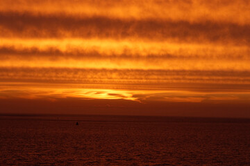Fiery orange sunset over a calm, dark ocean.  Striated clouds paint the sky.  Tranquil scene.