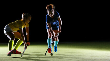 Female players engage in competitive field hockey match in contrast studio light