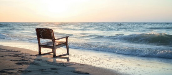 Solitary wooden chair on a serene beach at sunset with gentle waves lapping at the shore creating a tranquil atmosphere.