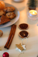 Various Christmas decorations, cookies, chocolate, nuts and tangerines, wine glasses and lit candles on the table. Holiday hygge at home. Selective focus.