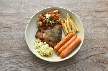grilled pork steak dressing gravy sauce with French fries and chop cabbage salad couple sausage on plate 