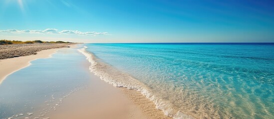Obraz premium Tranquil clear water beach with gentle waves and a vibrant blue sky on a serene island coastline