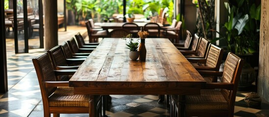 Fototapeta premium Elegant wooden dining table with cozy chairs in a lush, green indoor setting creating a warm and inviting atmosphere for gatherings